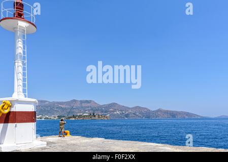 Mann Angeln von einem Kai, überschattet von einem Hafen-Licht, mit Hügeln und Stadt in der Ferne. Stockfoto