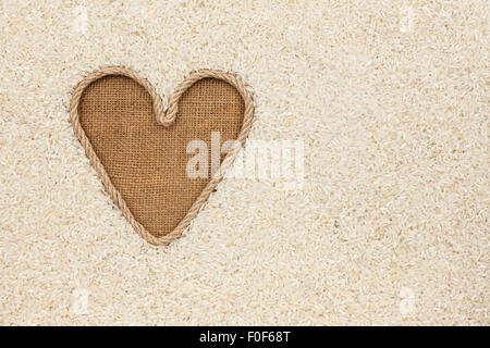 Das symbolische Herz des Seils liegt auf Sackleinen und Reis Getreide, mit Platz für Ihren text Stockfoto