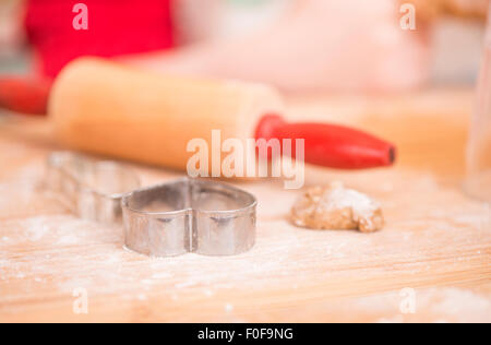 Ausstecher, Lebkuchen-Cookie-Teig und Nudelholz auf Holzbrett. Junges Mädchen im Hintergrund. Stockfoto