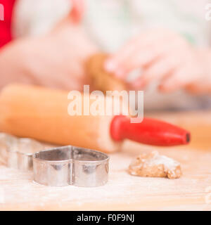 Ausstecher, Lebkuchen-Cookie-Teig und Nudelholz auf Holzbrett. Junges Mädchen im Hintergrund. Stockfoto