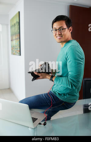 Chinesischer Mann verbindet digitale Dslr-Kamera, Laptop-Computer über USB-Kabel, Fotos und Videos auf PC. Der Mann sitzt auf t Stockfoto