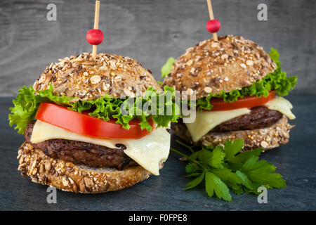 Zwei Gourmet-Hamburger mit Käse und frischem Gemüse auf Mehrkorn Brötchen auf dunklem Hintergrund Stockfoto