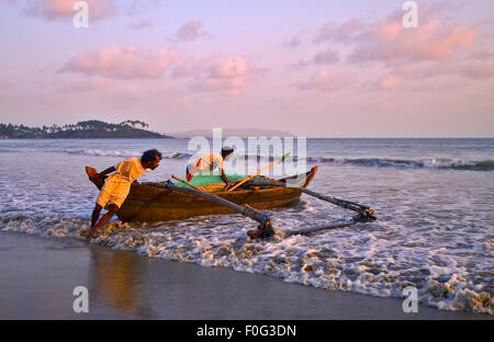 Zwei lokale Fischer startet ihre Holzboot bei Sonnenuntergang am Palolem Beach, Goa in Südindien. Stockfoto