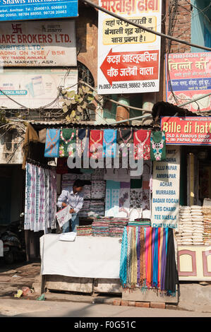 Amritsar, Punjab, Indien. Straßenbild; bunte am Straßenrand Stall zu verkaufen T-shirts, Tischdecken und andere Textilien mit einem Durcheinander von Handel Zeichen oben in westlichen und Hindi Schrift. Stockfoto