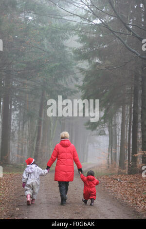 Mutter mit zwei Kindern auf einem Pfad in einem Wald im Winter vor Weihnachten. Eines der Mädchen mit Skt Klaus Hut Stockfoto