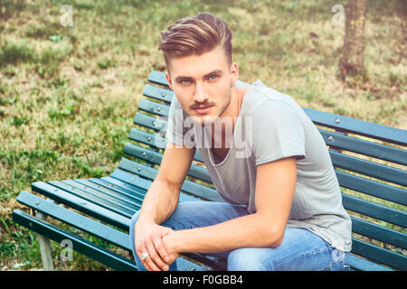 Hübscher blonder junger Mann sitzt auf grün, hölzerne Parkbank Stockfoto