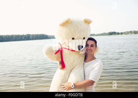 Hübscher junger Mann ist mit seinem massiven Teddybär herumalbern. Stockfoto