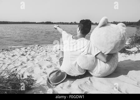 Hübscher junger Mann ist mit seinem massiven Teddybär herumalbern. Stockfoto