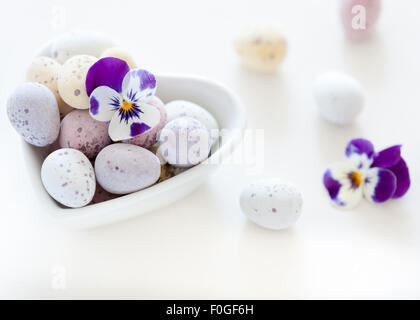 Mini Ostereier und Frühlingsblumen in eine herzförmige Schüssel Stockfoto