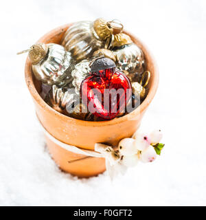 ein kleine Terrakotta-Topf gefüllt mit Christbaumkugeln und dekoriert mit einem Zweig von Snowberry, auf dem Schnee, Stockfoto