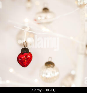 Nahaufnahme von einem herzförmigen roten Glas Christbaumkugel mit silbernen Kugeln und Bokeh im Hintergrund Stockfoto