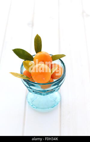 Vollreife haben, Kumquat, Citrofortunella Microcarpa in eine Glasschüssel auf Holzbrett Stockfoto