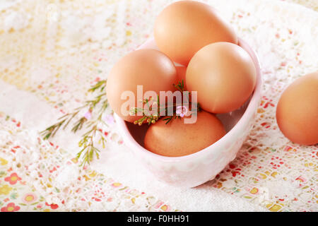 Braunen Eiern in einer Porzellanschüssel auf Spitze und Blumen Hintergrund Stockfoto