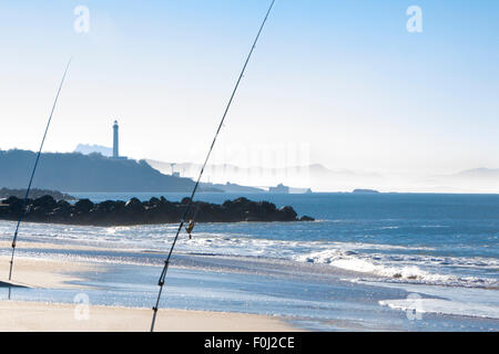 Angelruten in Aktion am frühen Nachmittag auf der Cote Basque in Biarritz mit dem Leuchtturm und dem Strand im Hintergrund. Stockfoto