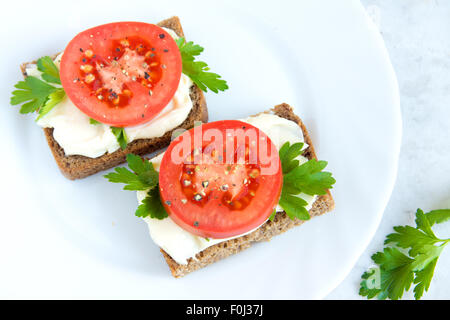 Sandwiches mit Tomaten, Frischkäse, Petersilie und Pfeffer auf weißen Teller Stockfoto