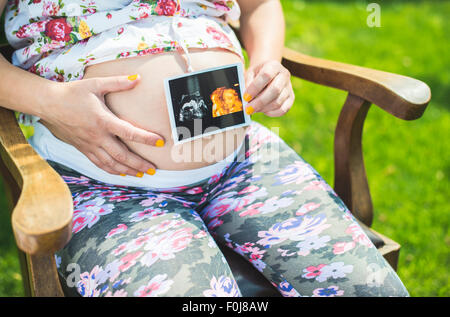Schwangere Frauen halten Bild der Gebärmutter. Tageslicht im Garten Stockfoto
