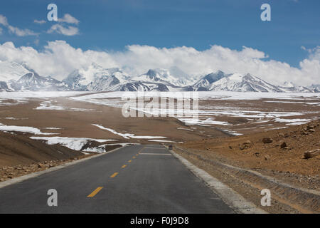 Gerade Straße mit einer gelben gepunkteten Linie in der Mitte mit tibetischen Landschaft der Berge im Hintergrund. Stockfoto