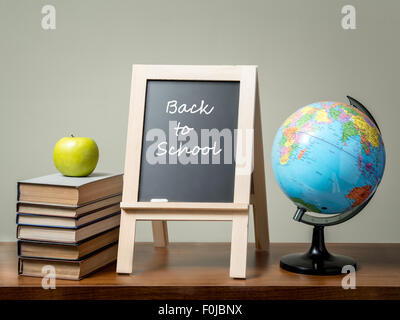 Stapel Bücher mit grünem Apfel, Globe und Tafel mit Back to School Satz alle über grüne Wand auf braunen Schreibtisch gelegt. Stockfoto