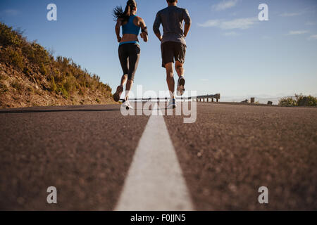Rückansicht von zwei jungen Menschen, die unterwegs zusammen zu trainieren. Mann und Frau am Morgen laufen auf Sommertag. Niedrigen Winkel Schuss von paar jo
