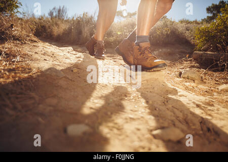 Wanderschuhe in Aktion auf einem Feldweg Trail. Nahaufnahme der männlichen Wanderer Schuhe auf Schmutz Weg. Junge Leute Wandern an einem sonnigen Tag. Stockfoto