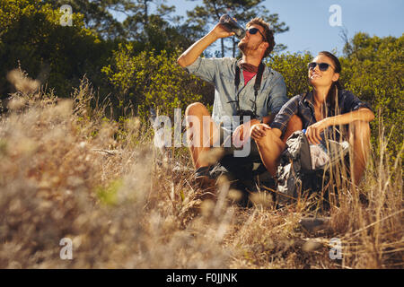 Im Freien Schuss des jungen Paares sitzen gemeinsam eine Pause auf Wanderung. Kaukasischen Mann und Frau Trinkwasser während Sie wandern. Stockfoto