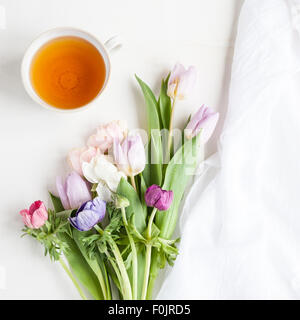 Blick von oben auf einen Haufen Frühlingsblumen, Anemonen und Tulpen, mit einer Tasse Tee und etwas Stoff, auf weißem Hintergrund Stockfoto