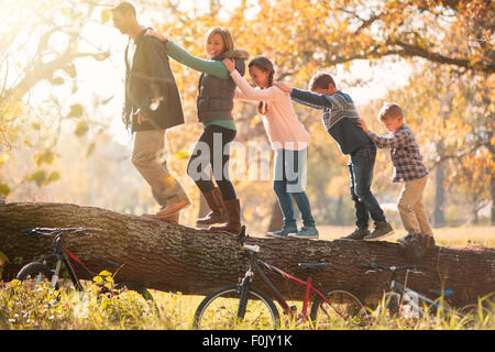 Familie gehen in einer Reihe auf umgestürzten Baumstamm in der Nähe von Fahrrädern Stockfoto