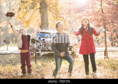 Jungen und Mädchen werfen Herbstlaub overhead im Wald Stockfoto