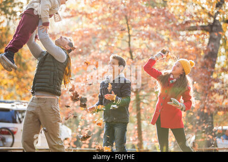 Verspielte Vater und Kinder spielen im Herbstlaub Stockfoto