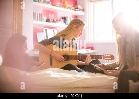 Mädchen im Teenageralter Gitarre zu spielen und mit digital-Tablette auf Bett Stockfoto
