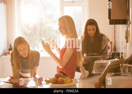 Mädchen im Teenageralter Magazin lesen, SMS und Verwendung von digital-Tablette in Küche Stockfoto