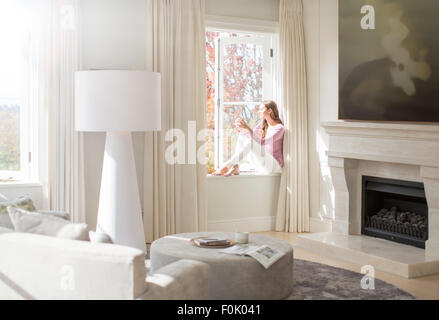 Frau sitzt auf der sonnigen Fensterbank Stockfoto