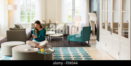 Frau SMS auf Handy auf Ottomane im Wohnzimmer Stockfoto
