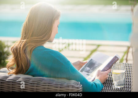 Brünette Frau liest am Luxus Pool Magazin Stockfoto