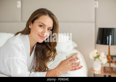 Lächelnde Frau Porträt im Bademantel Kaffeetrinken auf Bett Stockfoto