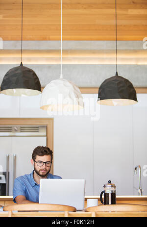 Mann mit Laptop unter Pendelleuchten in Küche Stockfoto