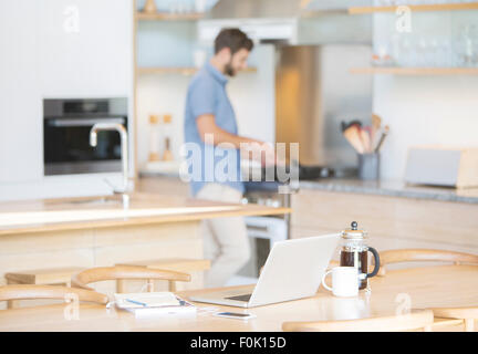 Mann am Herd hinter Kaffee, Laptop und Handy in Küche kochen Stockfoto