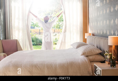 Frau im Bademantel Schlafzimmer Vorhänge öffnen Stockfoto