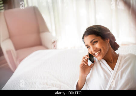Lächelnde Frau in Bademantel reden über Handy auf Bett Stockfoto