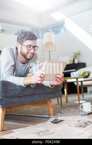 Mann mit Kopfhörern zu legen und mit digital-Tablette in Wohnzimmer Stockfoto