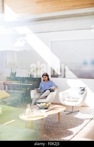 Frau liest Magazin im sonnigen Wohnzimmer Stockfoto