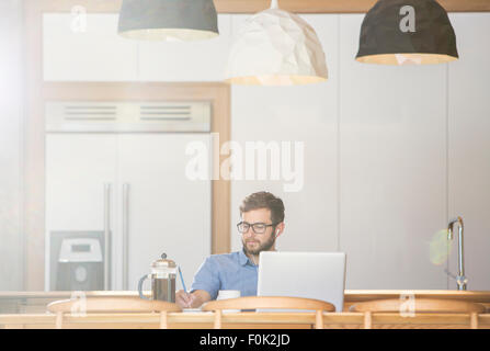 Mann am Laptop in der Küche mit französischen Presse Kaffee schreiben Stockfoto