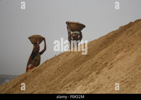 Männliche und weibliche Arbeiter tragen schwere Lasten von Sand auf ihre Köpfe in die Bank von Turag River bei Gabtoli in Dhaka ausgeglichen. Stockfoto