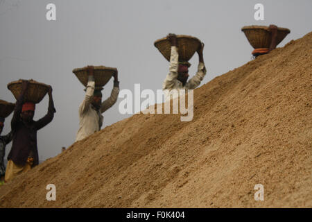 Männliche und weibliche Arbeiter tragen schwere Lasten von Sand auf ihre Köpfe in die Bank von Turag River bei Gabtoli in Dhaka ausgeglichen. Stockfoto