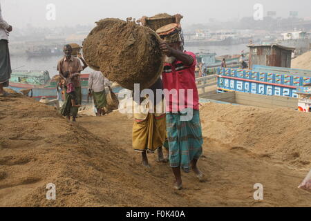 Männliche und weibliche Arbeiter tragen schwere Lasten von Sand auf ihre Köpfe in die Bank von Turag River bei Gabtoli in Dhaka ausgeglichen. Stockfoto