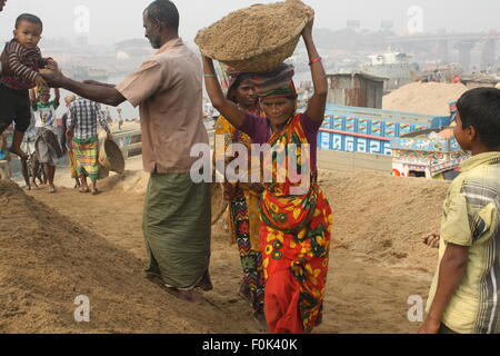 Männliche und weibliche Arbeiter tragen schwere Lasten von Sand auf ihre Köpfe in die Bank von Turag River bei Gabtoli in Dhaka ausgeglichen. Stockfoto