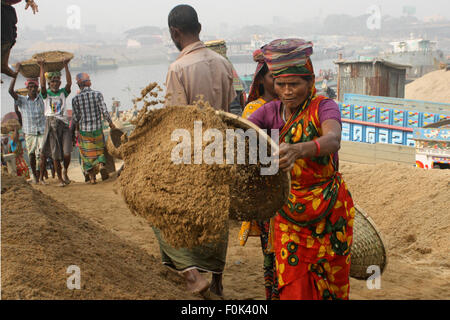 Männliche und weibliche Arbeiter tragen schwere Lasten von Sand auf ihre Köpfe in die Bank von Turag River bei Gabtoli in Dhaka ausgeglichen. Stockfoto