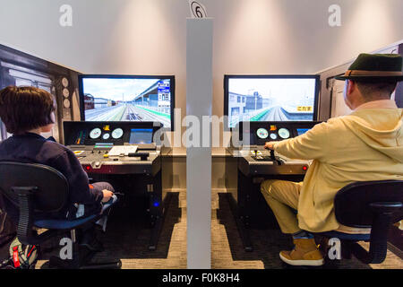 Japan, Nagoya, Railway Park. Shinkansen Museum. Blick über die Schulter eines japanischen Mann und ein Junge an zwei Zug Fahrsimulatoren Seite an Seite sitzen. Stockfoto