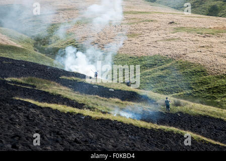 Brennen Sie Gräser auf die Mauren über Glossop in Derbyshire. Männer gegen den Rauchen-Rasen. Rahmen der Heidelandschaft. Stockfoto