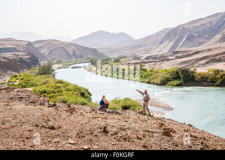 Touristen ang Führung am Ufer des Cunene Flusses (oder Kunene Fluss), bildet die Grenze zwischen Namibia und Angola, mit dürren Wüste Landschaft Stockfoto